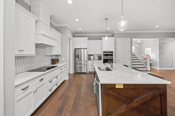 a large kitchen with kitchen island a stove a sink a refrigerator and white cabinets with wooden floor