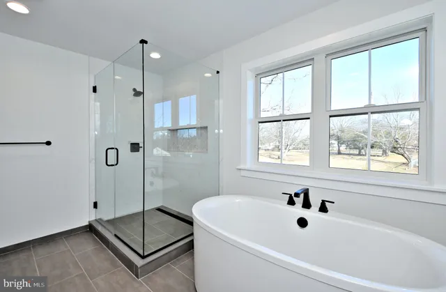 a bathroom with a tub a window and a glass door shower