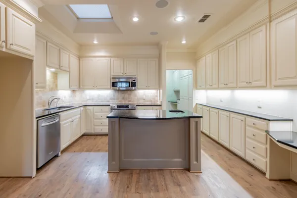 a kitchen with stainless steel appliances white cabinets a sink a stove a refrigerator and microwave with wooden floors