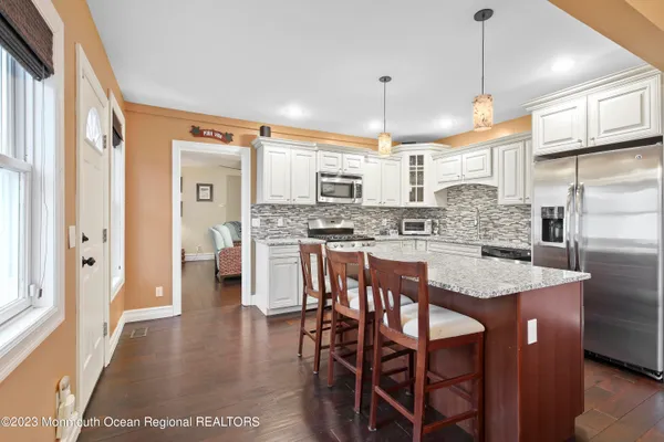 a kitchen with stainless steel appliances granite countertop a sink a stove a refrigerator and island with wooden floor