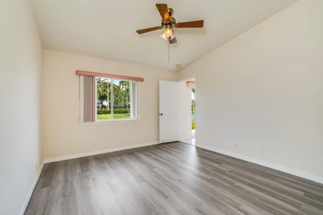 an empty room with wooden floor chandelier fan and windows
