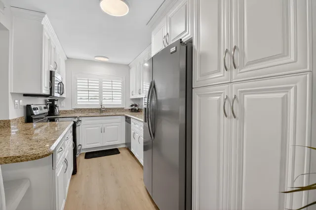 a kitchen with stainless steel appliances granite countertop a refrigerator a sink and white cabinets