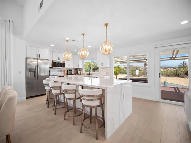 a kitchen with stainless steel appliances kitchen island granite countertop a refrigerator a oven a sink a dining table and chairs with wooden floor