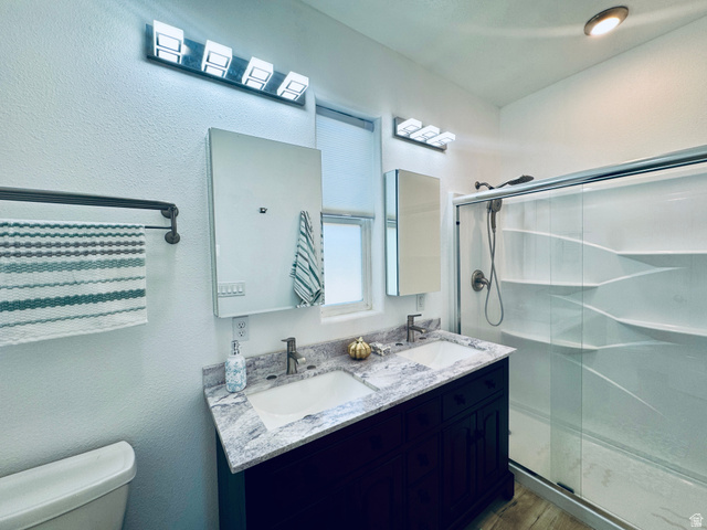 150 North 3050 East, Unit 4 St. George, UT 84790 - Photo 14 of 24 Bathroom featuring a dual sink vanity with a stone-finish countertop, dark wood cabinetry, two mirrored medicine cabinets, and a walk-in shower with a sliding glass door