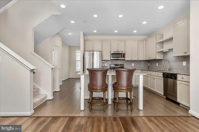 a kitchen with stainless steel appliances granite countertop a stove a sink a microwave a refrigerator and white cabinets with wooden floor