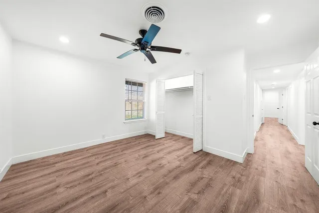 an empty room with wooden floor fan and windows