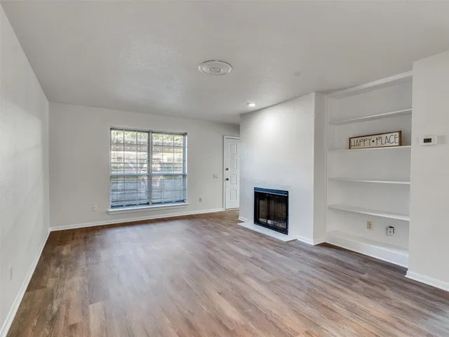 an empty room with wooden floor fireplace and windows