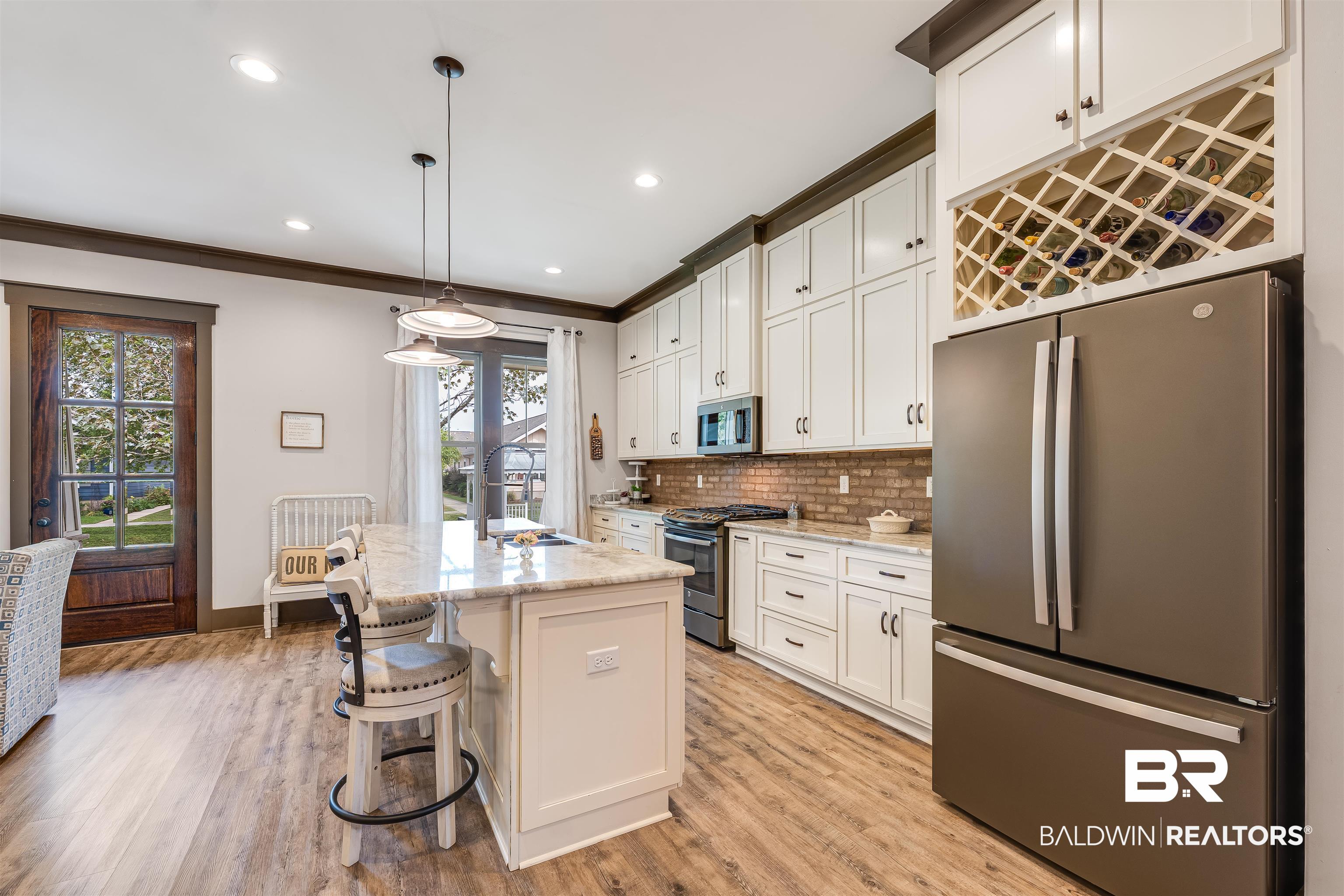 1119 Pink Poppy Lane Foley, AL 36535 - Photo 24 of 38 Kitchen with appliances with stainless steel finishes, white cabinetry, light stone countertops, a kitchen bar, and decorative backsplash