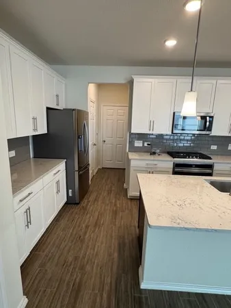 a kitchen with stainless steel appliances a stove a sink a refrigerator white cabinets and wooden floor
