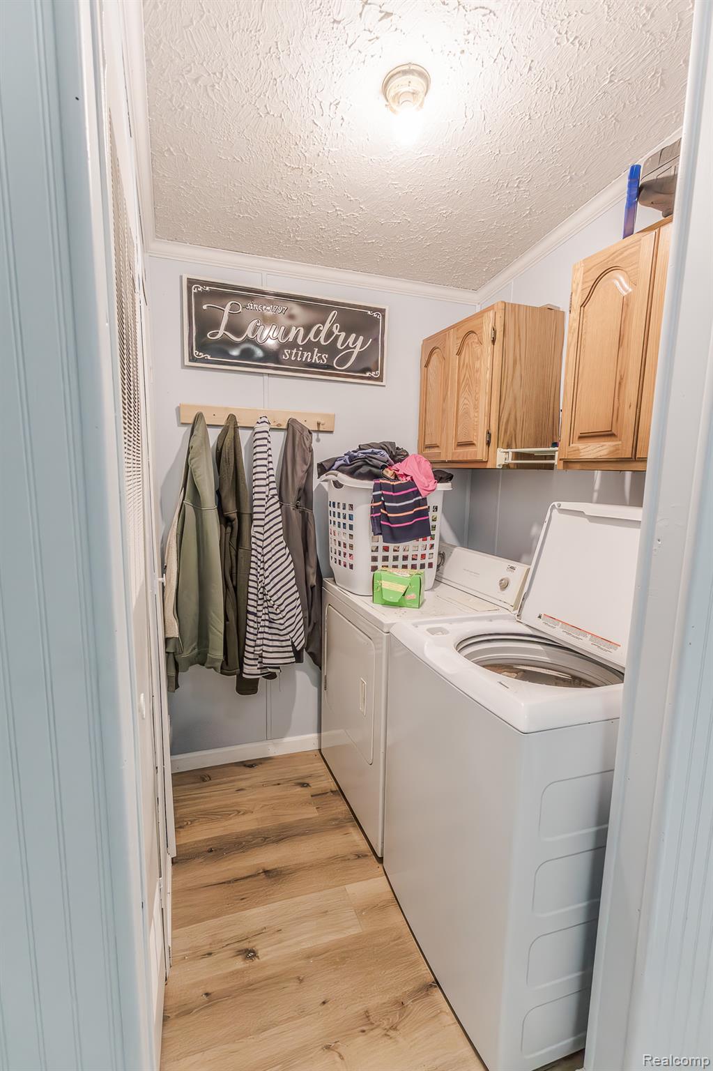 2649 Brown Road Millington, MI 48746 - Photo 9 of 18 Dedicated laundry room featuring white stackable washer and dryer units, wood-finish cabinetry with arched door fronts, countertop workspace, wall-mounted clothing rod, and wood-finish flooring throughout