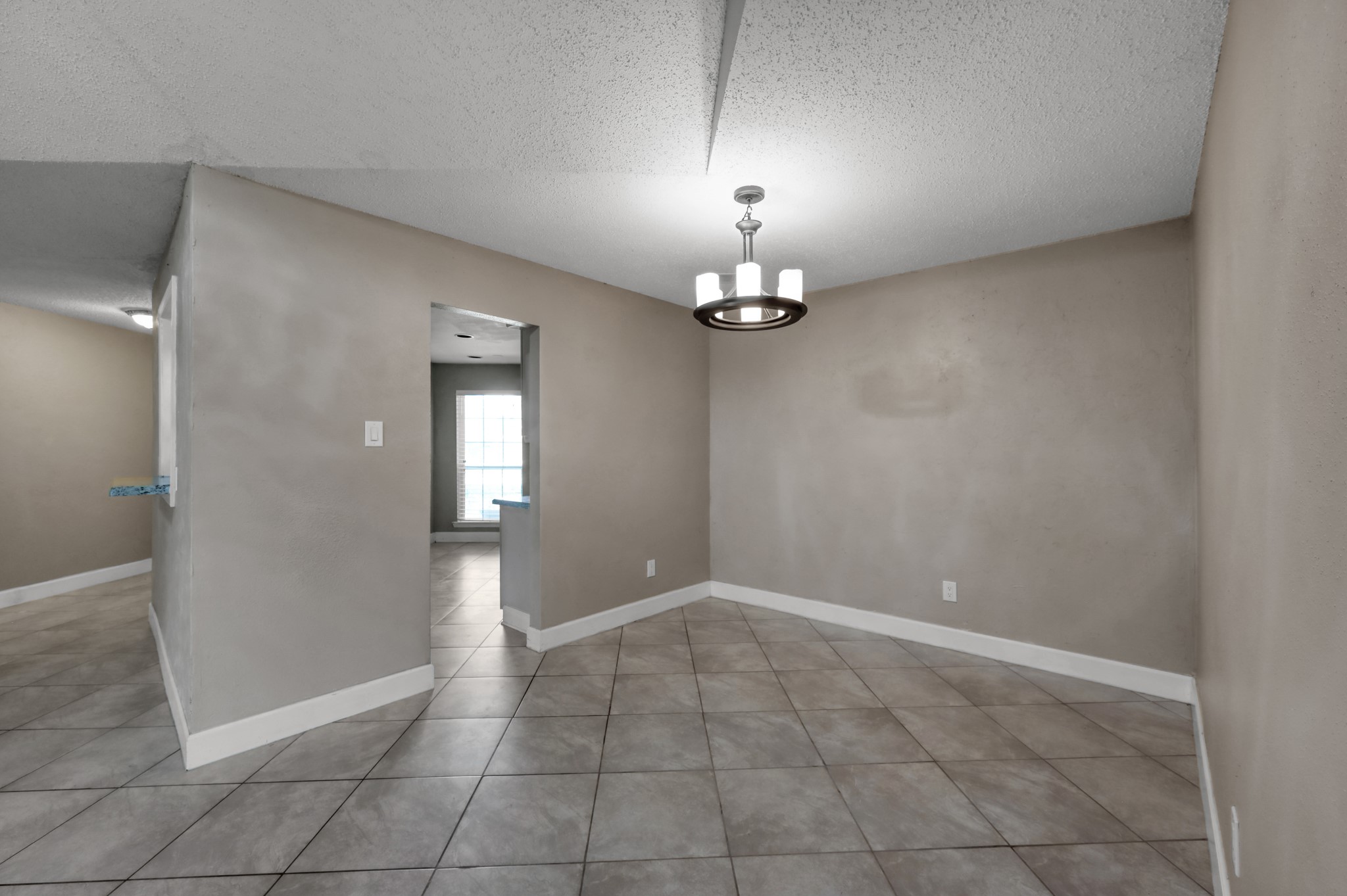 12015 Fallbrook Drive Houston, TX 77065 - Photo 10 of 29 This photo features a tiled room with neutral-colored walls and a modern light fixture. It opens into another space with natural light from a window. The layout offers a versatile area for dining or living use.
