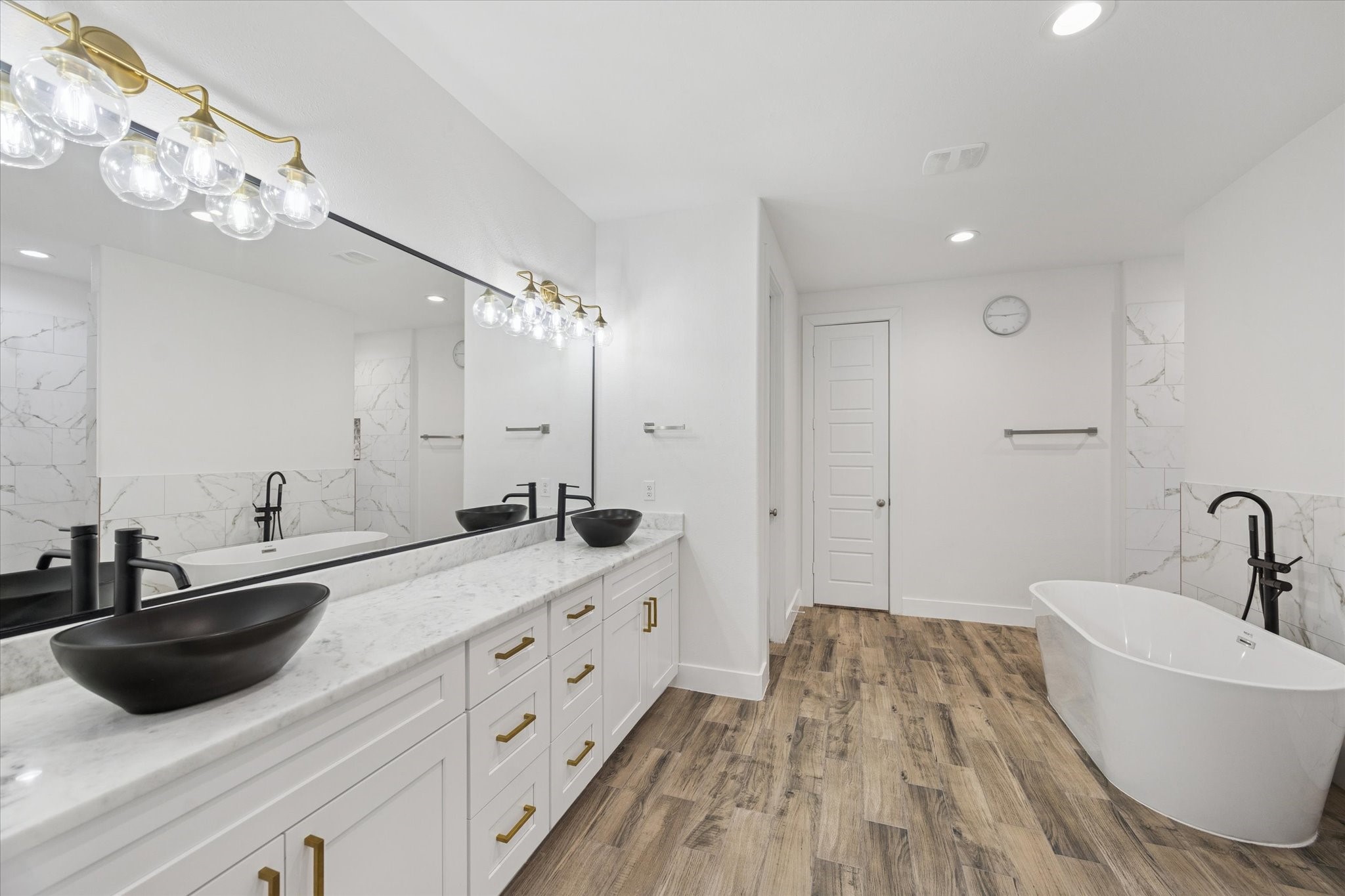 203 Hampton Glen Road Montgomery, TX 77356 - Photo 15 of 28 This ensuite bathroom showcases elegance and thoughtful design in every detail. The marble countertops, custom mirrors, and brass LED light fixtures create a sophisticated, harmonious look. Recently installed dark sinks and black faucets add striking contrast while enhancing the overall aesthetic, making this space both functional and exceptionally refined.