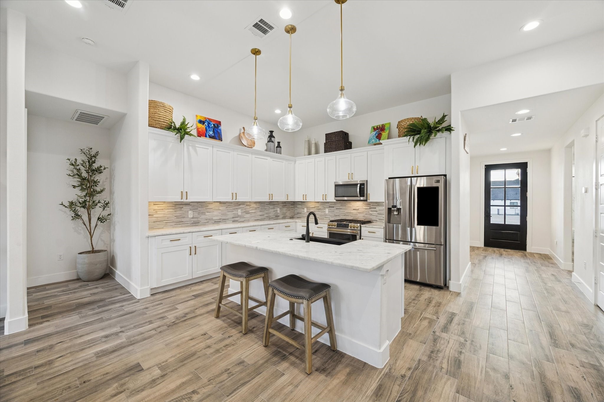 203 Hampton Glen Road Montgomery, TX 77356 - Photo 8 of 28 This kitchen view showcases the stunning backsplash and under-cabinet lighting, adding refined elegance to the space. The LED and pendant lights create a beautifully layered ambiance, perfectly complemented by abundant natural light and a soft, sophisticated color palette. A recently installed Litchen-Karran Farmhouse apron-front sink (34" x 21.25", single bowl, quartz) adds both style and functionality, enhancing the kitchen’s luxurious and inviting atmosphere.