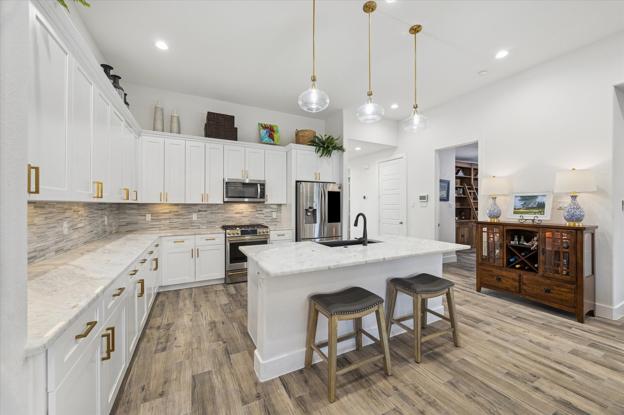 203 Hampton Glen Road Montgomery, TX 77356 - Photo 9 of 28 This view highlights the marble countertops, elegant backsplash, and the kitchen island with space for stools, perfect for enjoying conversation with guests while entertaining. The thoughtful layout and placement of elements in this space create a functional yet sophisticated environment, making the kitchen as stylish as it is inviting.