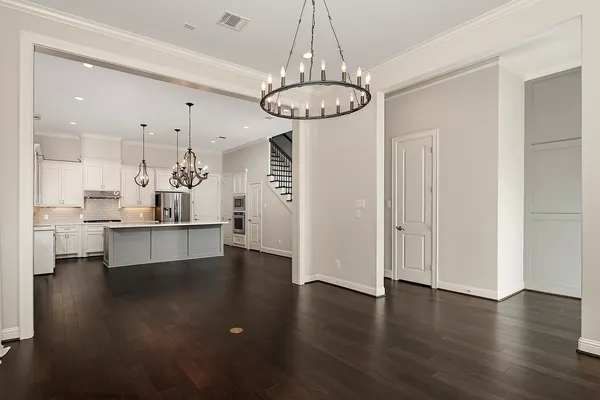 a view of an empty room and kitchen with wooden floor