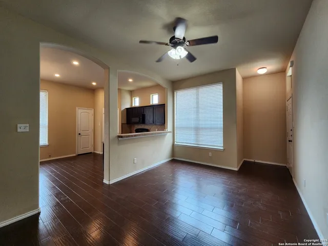 a view of an empty room with wooden floor and a kitchen