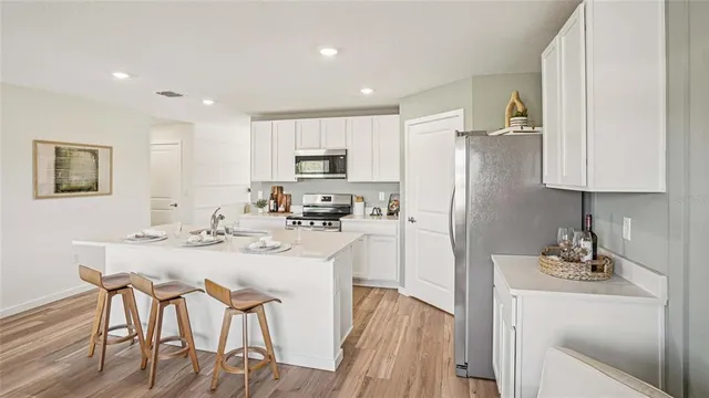 a kitchen with stainless steel appliances kitchen island granite countertop a refrigerator a stove a sink a dining table and chairs with wooden floor