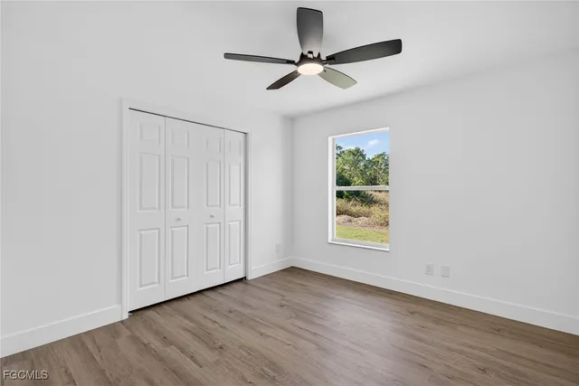 an empty room with wooden floor chandelier fan and windows