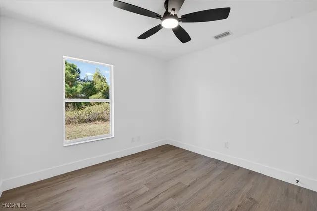 an empty room with wooden floor ceiling fan and windows