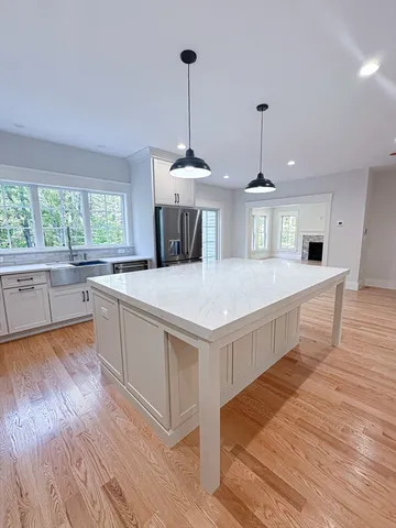 a large white kitchen with granite countertop a stove a sink dishwasher a kitchen island with wooden floor and cabinets
