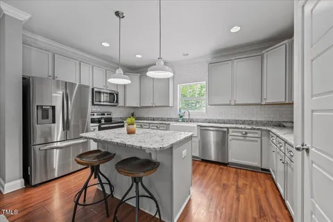 a kitchen with granite countertop a refrigerator a stove a sink and white cabinets with wooden floor