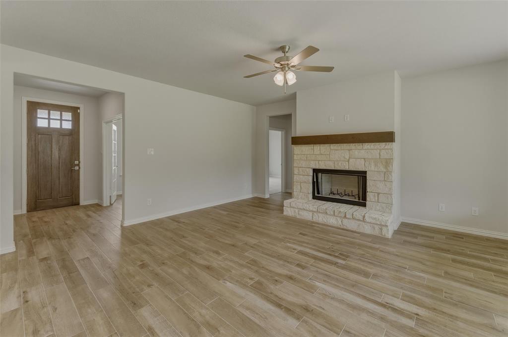 156 Oak Grv Way Springtown, TX 76082 - Photo 9 of 25 Spacious living area featuring wood-finish flooring, a stone fireplace with a wood mantel, a ceiling fan, and a paneled entry door with transom window