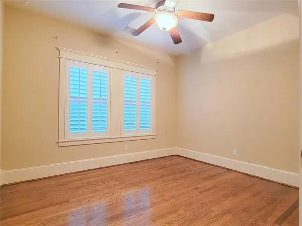 an empty room with wooden floor chandelier fan and windows