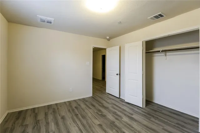 a view of an empty room with wooden floor and closet