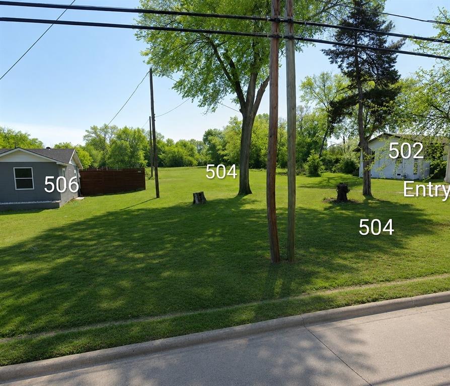504 North Hampton Road DeSoto, TX 75115 - Photo 8 of 11 Expansive grassy lot featuring mature trees, a paved curb, and clear skies