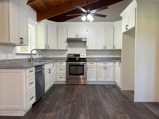 a kitchen with granite countertop white cabinets and a stove with wooden floor