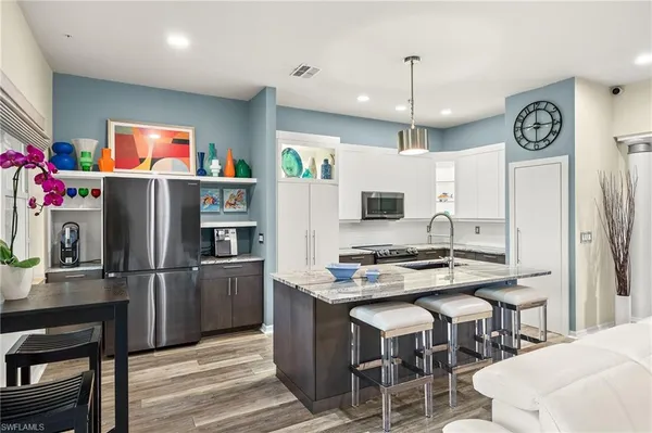 a kitchen with stainless steel appliances granite countertop a refrigerator a sink dishwasher a stove a dining table and chairs with wooden floor