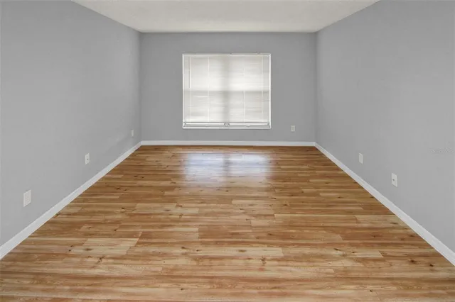 a view of an empty room with wooden floor and window