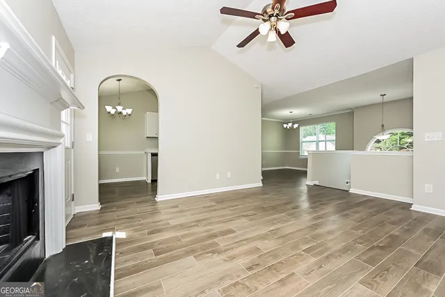 a view of an empty room and kitchen with a fireplace wooden floor