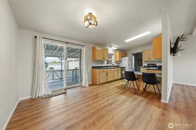 a kitchen with stainless steel appliances granite countertop a refrigerator a stove top oven a dining table and chairs with wooden floor