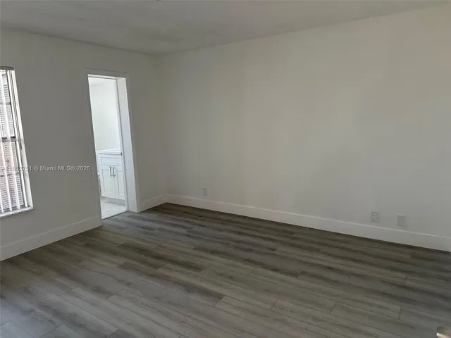 a view of an empty room with wooden floor and window