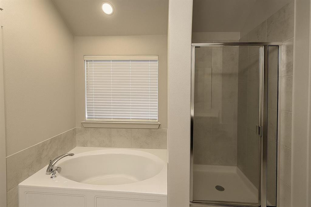 5641 Durst Lane Forney, TX 75126 - Photo 6 of 10 Bathroom featuring a built-in soaking tub with chrome fixtures, a window with horizontal blinds, and an adjacent enclosed shower with a glass door and tiled walls