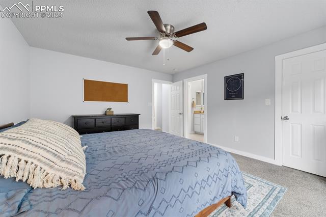 7730 Julynn Road Colorado Springs, CO 80919 - Photo 15 of 48 Carpeted bedroom featuring a textured ceiling, connected bathroom, and ceiling fan