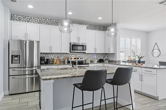 a kitchen with stainless steel appliances granite countertop a sink a stove a refrigerator cabinets and chairs