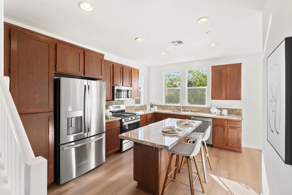 1276 San Elijo Road North San Marcos, CA 92078 - Photo 5 of 35 a kitchen with a refrigerator a stove a sink dishwasher and a dining table with wooden floor
