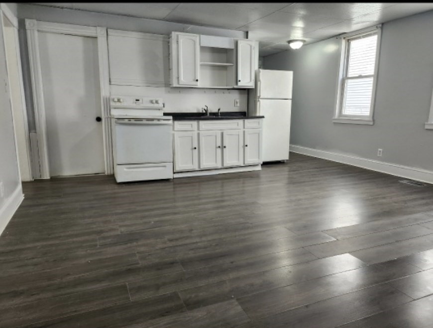 a kitchen with stainless steel appliances granite countertop a coffee maker a sink with white cabinets and wooden floor