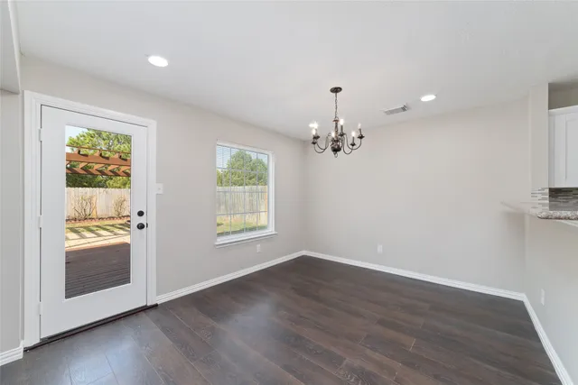 an empty room with wooden floor chandelier and windows