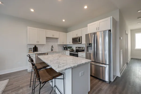 a kitchen with stainless steel appliances granite countertop a stove top oven a sink dishwasher and a refrigerator with wooden floor