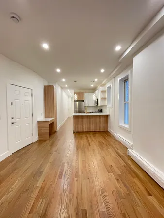 a view of an empty room with wooden floor and kitchen