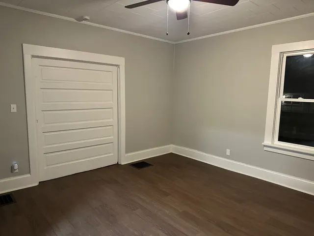 an empty room with wooden floor closet and windows