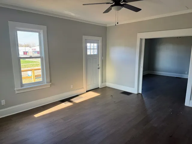 an empty room with wooden floor chandelier fan and windows