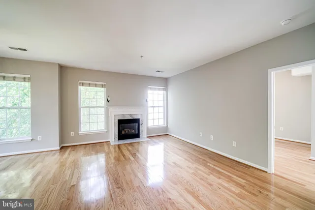 an empty room with wooden floor fireplace and windows