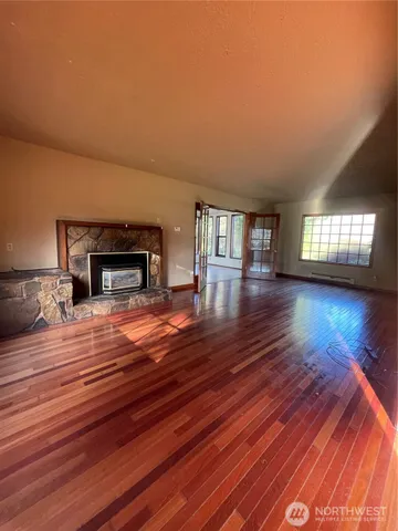 a empty room with wooden floor fire place and windows