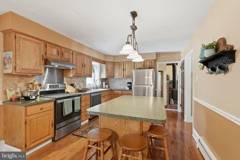 a kitchen with stainless steel appliances granite countertop a stove top oven a sink a dining table and chairs with wooden floor