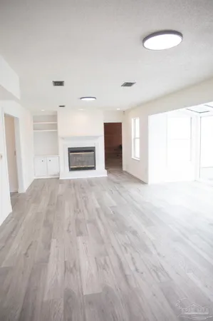 an empty room with wooden floor fireplace and windows