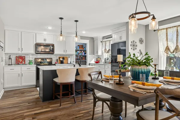 a kitchen with stainless steel appliances granite countertop a dining table chairs refrigerator and sink